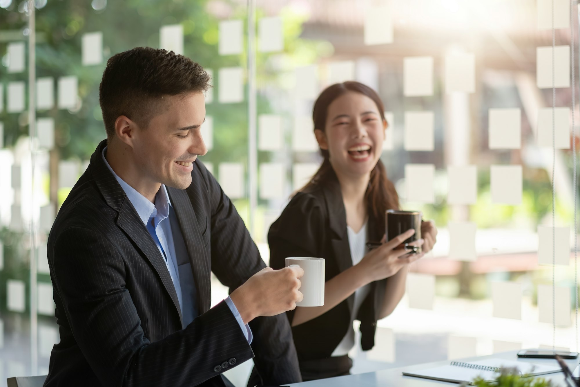 Friendly male leader laughing at group business meeting, happy young businesswoman enjoying fun