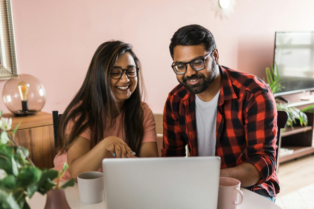 Latino or indian man and woman couple use their laptop in the living room to make video calls. Video