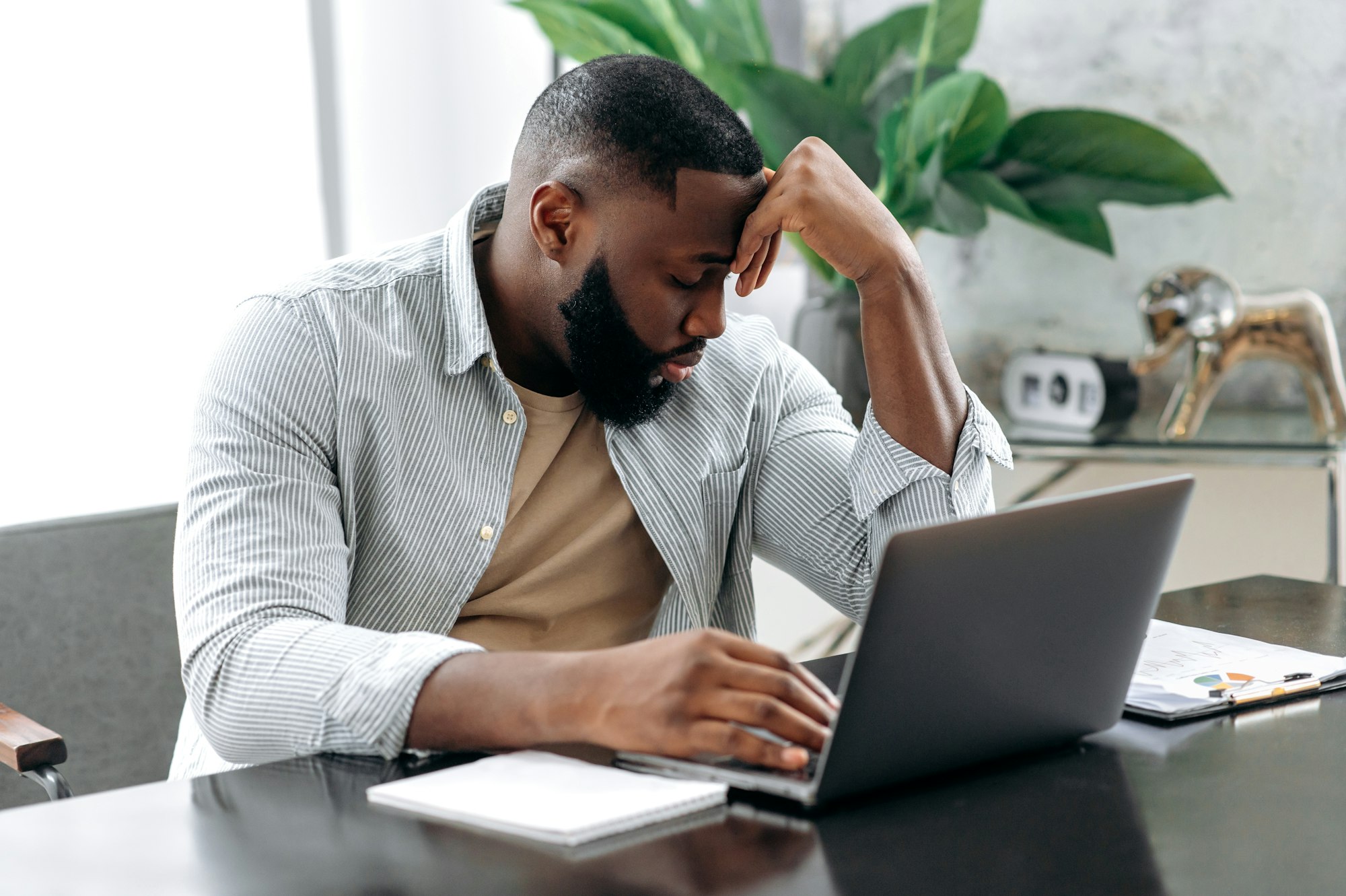 Sad exhausted african american young man, company employee, sitting at a desk, looks tired and