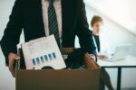 male employee standing holding office supplies in the paper box going to submit a resignation